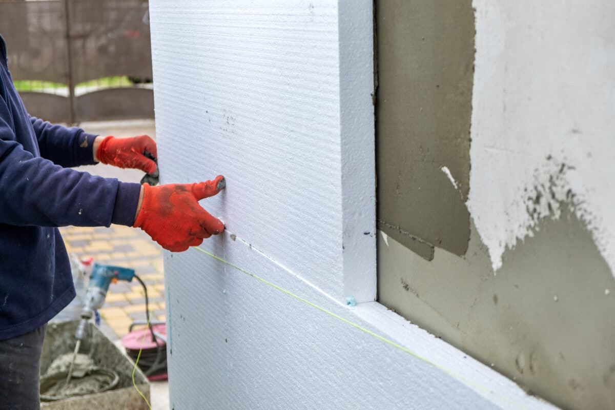 construction worker installing styrofoam insulation sheets on house facade wall for thermal protection.
